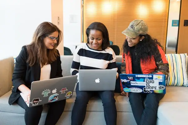 three women with their laptops, sitting beside each other and having a conversation